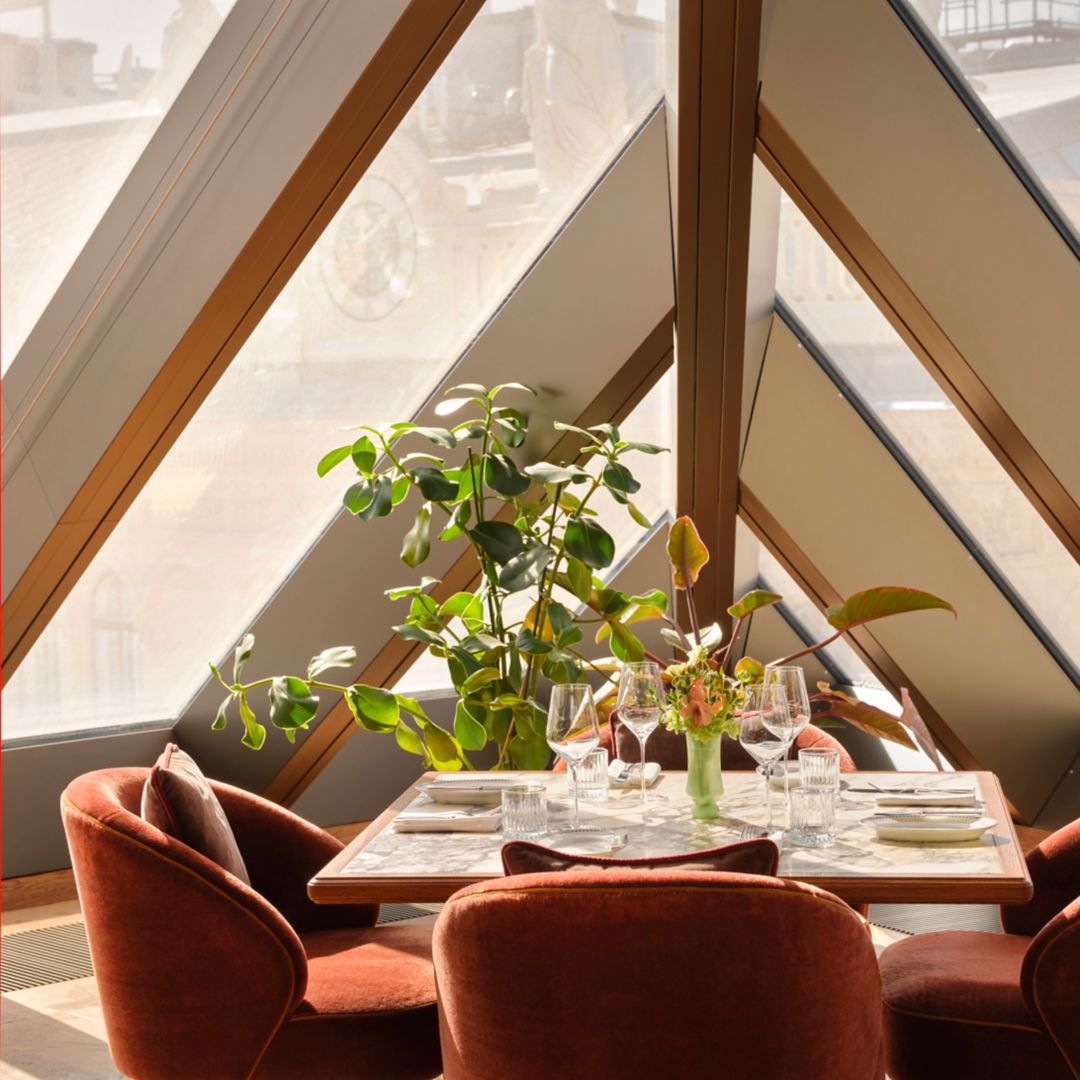 A dining table set with wine glasses, plates, and a flower arrangement, surrounded by chairs.